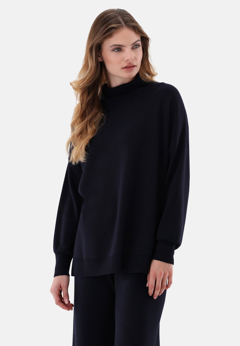 Marineblauer übergroßer Pullover mit hohem Kragen, weiten Ärmeln, gerippten Bündchen und Saum, aus weichem Stoff, kombiniert mit passenden Hosen.
