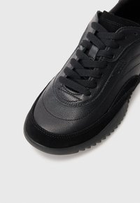 Μαύρο δερμάτινο αθλητικό παπούτσι με απαλό φινίρισμα, υφασμάτινες μαύρες σουέτ λεπτομέρειες, στρογγυλή μύτη και μαύρα επίπεδα κορδόνια με λάστιχο σόλας.