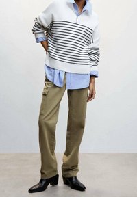 Maglione bianco a righe con zip, indossato sopra una camicia button-up azzurro chiaro, abbinato a pantaloni cargo khaki e stivali neri con tacco.