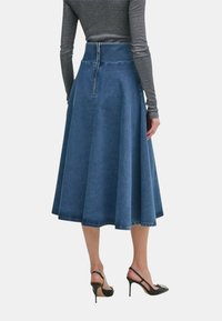 Denim A-line nederdel, mørkeblå, knælang, talje med lynlås bagpå. Sammen med slanke sorte højhælede sko. Glat tekstur.
