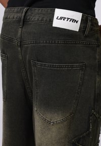 Black denim jeans with a light faded finish, featuring a distressed accent, two back pockets, and a white label with "URTRN" on the waistband.