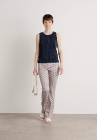 Mouwloze marineblauwe top met verticale textuurlijnen, gecombineerd met lichte, gemusterde broeken met cirkels. Accessoires omvatten een lichte handtas.