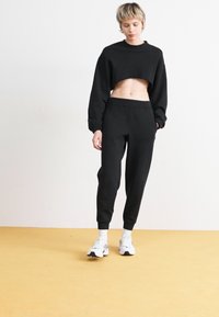 Svart avkortet genser og svarte joggebukser i mykt stoff. Genseren har rund hals og lange ermer med elastiske mansjetter.