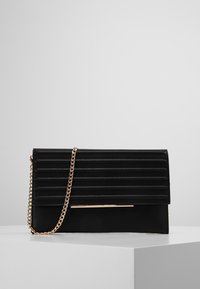 Svart kuvertväska med horisontella veck, guldig kedjehandtag som hänger över framsidan, och en tunn guldaccentstång på framsidan, på vit yta.