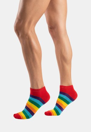 Naga noga w kolorowych skarpetkach w paski tęczy, z czerwonymi mankietami, piętami i palcami, stojąca na białym tle.