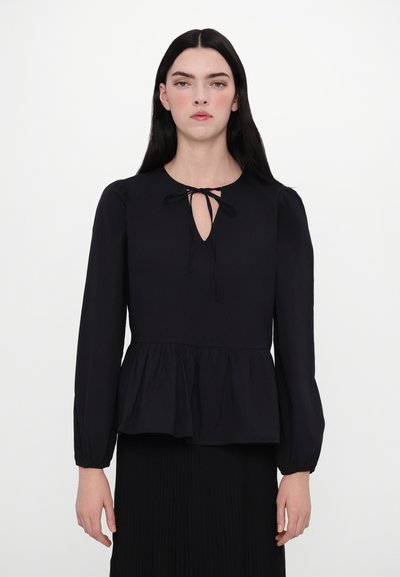 Zwarte peplum blouse met lange mouwen, sleutelgat halslijn vastgemaakt met een strik, gladde textuur en gathered zoom, gedragen over een geplooide rok.