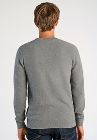 Pullover grigio a maglia con texture, colletto rotondo e maniche lunghe, con polsini e orlo a coste. Indossato sopra jeans in denim scuri.