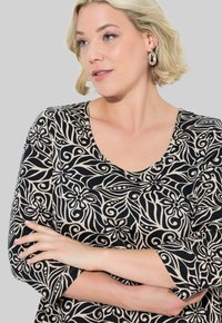 Blusa a fiori nera e beige con maniche a tre quarti, scollatura rotonda e una texture liscia. Presenta disegni botanici intricati.