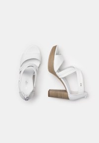 White high-heeled sandals with cross straps and a textured wooden heel. Smooth synthetic material with a zip closure at the back.