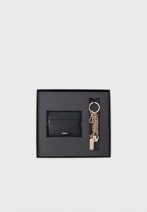 Porte-cartes en cuir noir avec logo "BOSS" et porte-clés doré orné de plusieurs breloques, présenté dans une boîte cadeau noire.