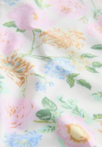 Tissu blanc doux avec un motif floral pastel comprenant des fleurs roses, jaunes, bleues et des feuilles vertes, présentant de légers plis et une texture délicate.