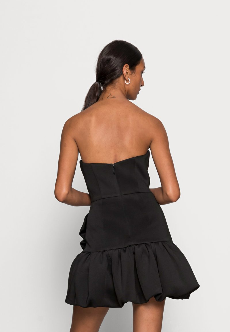 Abito nero senza spalline con corpino aderente e orlo arricciato. Tessuto morbido con chiusura a zip sul retro.