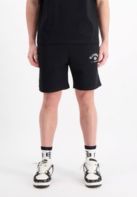 Zwarte shorts van een gladde stof, met een klein wit logo op het linkerpijp. Draag met zwarte sneakers en gemusterde sokken.