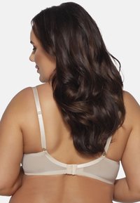 Reggiseno beige con una texture liscia, spalline regolabili e chiusura a gancio. Presenta un design minimalista e tessuto morbido.