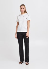 White cotton t-shirt with black bow embroidery, short sleeves, round neckline, paired with black tailored pants and black strappy sandals.