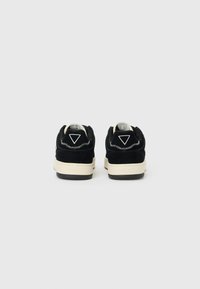 Black suede sneakers with white stitching, triangular logo, cream midsole, and black rubber outsole, featuring a simple design.