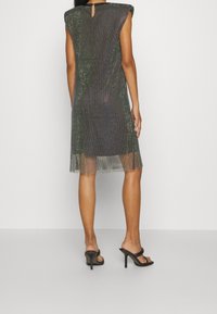 Průhledné černé síťované šaty s tečkovaným vzorem, s krátkým rukávem, detail s vytvarováním zad, do kolen, spárované s černými sandály na podpatku.