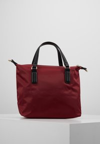 Borsa tote rossa in nylon con manici in pelle nera, forma rettangolare, texture liscia, dettagli in hardware dorato e chiusura con zip laterale.