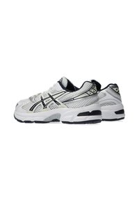 White athletic shoes with mesh upper, black accents, and metallic detailing. Features cushioned sole and lace-up design.