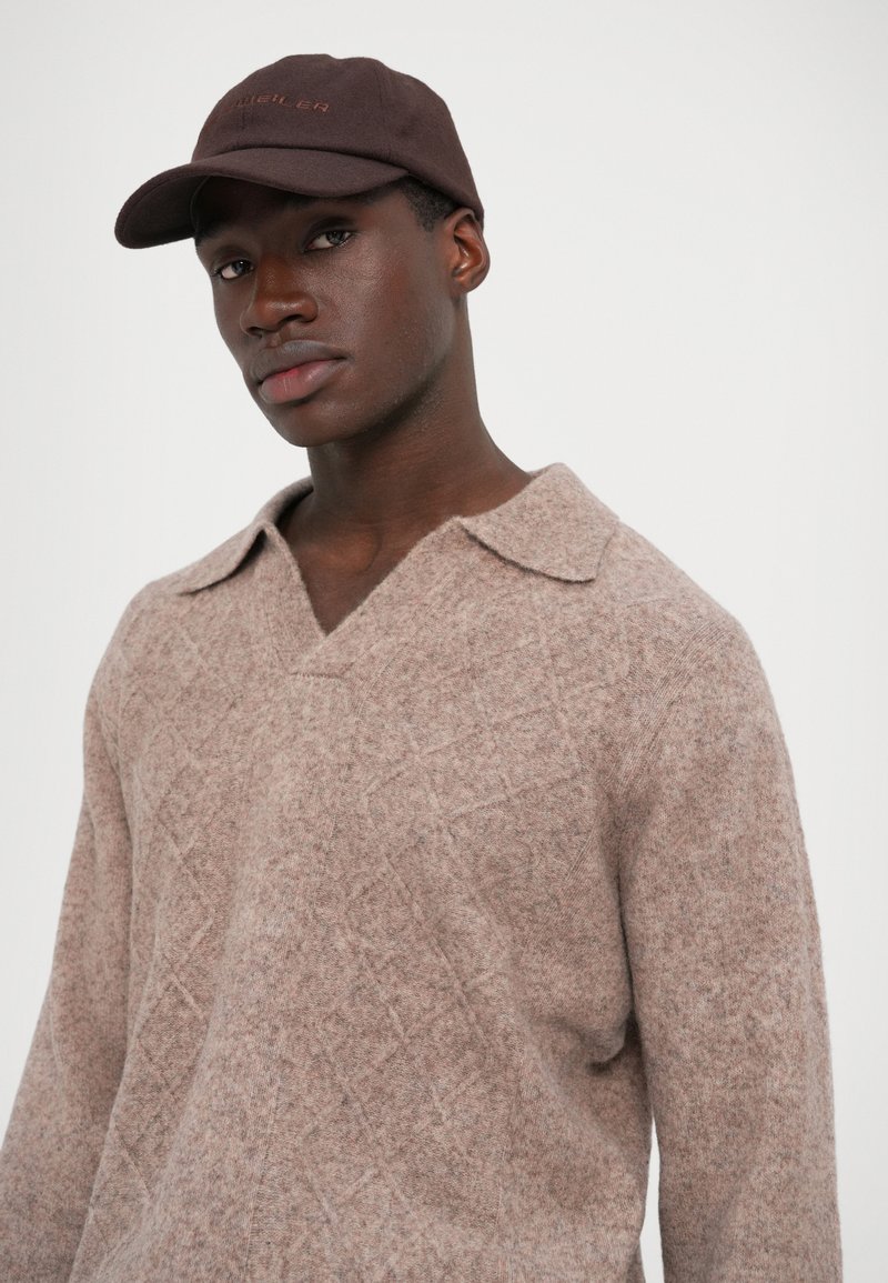 Pull en mélange de laine brun clair avec un motif diamant texturé, doté d'un col en V et d'un large col. Associé à une casquette brun foncé.