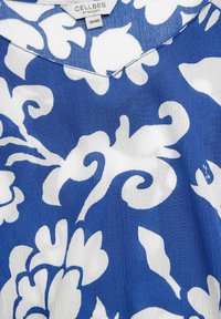 Blåt og hvidt blomsterprintet stof med V-hals design, glat tekstur og flydende fald. Etiketten siger "CELLBES OF SWEDEN."