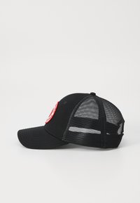 Svart caps med solid front og mesh bak. Har en rund rød lapp på fronten og en buet skygge. Teksturert stoff og justerbar stropp.