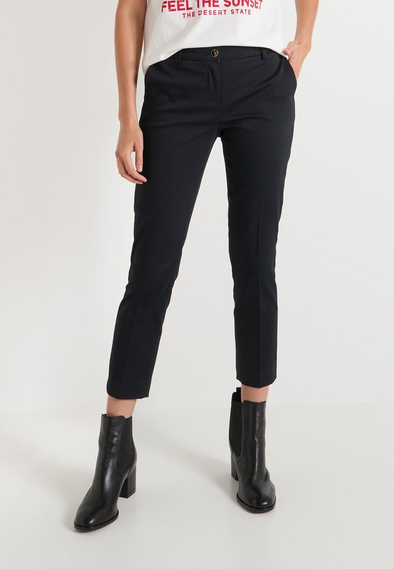 Pantalons chevilles noirs ajustés avec une coupe slim, poches avant et un léger éclat, assortis à des bottines noires élégantes.