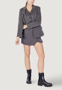 Giacca a righe grigia con gonna corta abbinata e stivali alla caviglia in pelle nera con suola testurizzata e dettagli con cerniera.