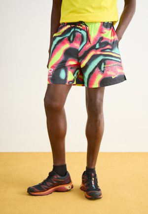 Multifarvede atletikshorts i et livligt svirvelmønster af rød, grøn og sort med en snøre i taljen og logoaccente; parret med sorte løbesko.