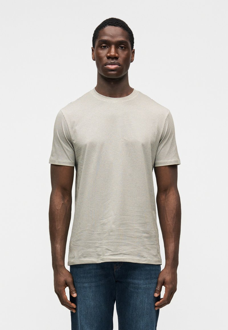 Ανοιχτό γκρι κοντομάνικη μπλούζα με υφασματικό μοτίβο, στρογγυλή λαιμόκοψη και χαλαρή εφαρμογή, συνδυασμένη με σκούρο μπλε τζιν παντελόνι.