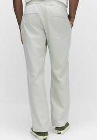Lichtgrijze, loszittende broek met een elastische tailleband en twee achterzakken. G gedragen met groene schoenen. Zacht, soepel materiaal.