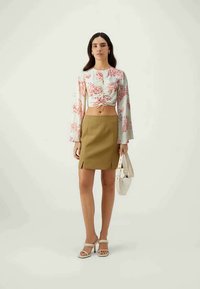 Top cropped fluido, branco, com padrão de coral vermelho, detalhe de laço frontal, combinado com uma saia mini justa verde-oliva e sandálias de bloco em tom bege.