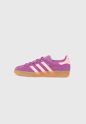 Fioletowe zamszowe buty sportowe Adidas Gazelle z różowymi paskami i wstawką na pięcie, gumową podeszwą oraz złotym napisem „Gazelle” z boku.