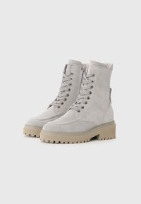 Graue Wildleder-Stiefeletten mit einer klobigen beigen Sohle, ausgestattet mit Schnürsenkeln und Metallösen. Abgerundete Spitze und gestickte Details an der Vorderseite.