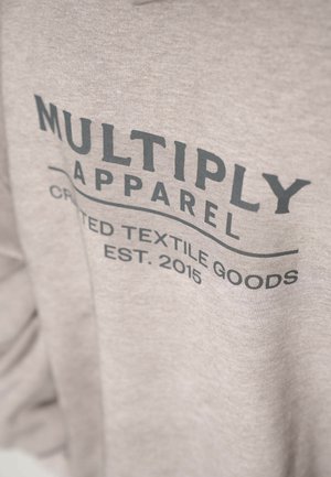 Sudadera gris hecha de un tejido suave; presenta un atrevido texto negro "MULTIPLY APPAREL" y "CRAFTED TEXTILE GOODS EST. 2015" en un diseño gráfico.