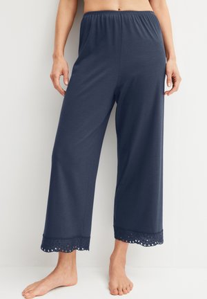 Marineblauwe wijde loungebroek met elastische tailleband en oogletkantafwerking bij de enkel, gedragen door een staand persoon zonder schoenen.