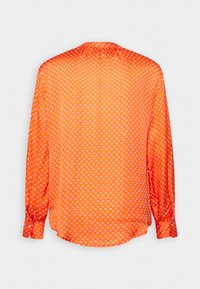 Blouse orange à manches longues avec des pois blancs, encolure froncée et poignets boutonnés, vue de dos sur fond blanc.