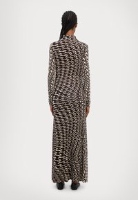Robe maxi longue à manches longues, avec un motif en zigzag noir et blanc, fabriquée à partir d'un tissu léger et texturé.