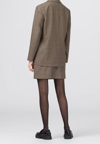 Blazer marron à carreaux associé à une jupe assortie ; texture lisse, coupe structurée, porté avec des chaussures noires et des collants.