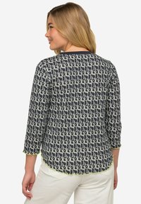 Blusa a motivi navy con un design geometrico, maniche a tre quarti e un orlo scallop lime verde. Il tessuto appare leggero.