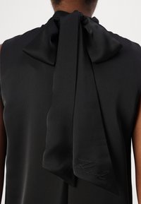 Svart ärmlös topp med en stor satinrosett på baksidan, med mjukt, slätt tyg och subtila broderade detaljer.