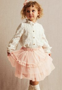 Hvid, broderet skjorte med lange ærmer, parret med en lagdelt, voluminøs pink tylskørt og knæhøje hvide strømper.