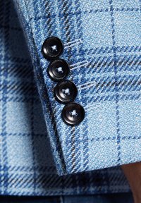 Niebieska tkanina w kratę z teksturowanym splotem i czterema czarnymi guzikami na mankiecie, prezentująca kontrastujące niebieskie i brązowe linie.