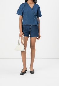 Denim wrap top with short sleeves, paired with dark denim shorts. Accessorized with a white handbag and black pointed toe heels.