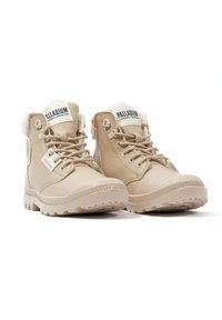 Botas de media altura en color beige, fabricadas en material sintético, con un forro suave, puntera redonda, cordones en la parte delantera y suela rugged con detalles de tracción.