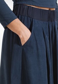 Marineblauwe corduroy rok met een geplooide elastische tailleband. Inclusief zijzakken en verticale ribbeltextuur, wat het algehele ontwerp versterkt.