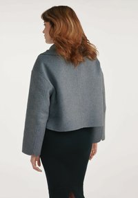 Szara krótka kurtka z mieszanki wełny o miękkiej teksturze; okrągły dekolt i szerokie rękawy, w połączeniu z prążkowaną czarną spódnicą z tylnym rozcięciem.