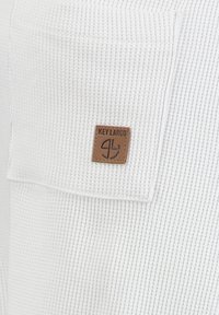 Tissu texturé blanc en gaufre avec une étiquette en cuir rectangulaire marron portant l'inscription "KEY LARGO" cousue à la surface.
