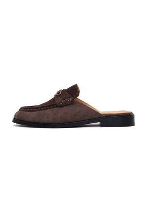 Mule en daim marron à enfiler avec un petit talon noir, bout arrondi, détails cousus et petite boucle dorée sur le dessus.