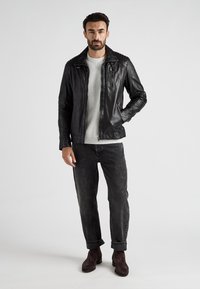 Svart läderjacka med dragkedjefickor, ribbade detaljer på axlarna, kombinerad med en ljusgrå tröja och mörk jeans, avslutad med bruna mockaboots.